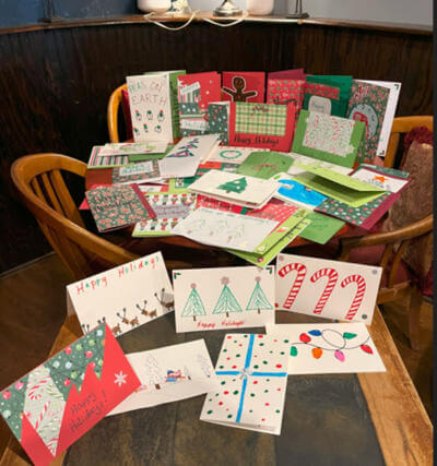 Una mesa de madera está llena de coloridas tarjetas navideñas hechas a mano con diseños festivos como árboles, bastones de caramelo y luces.