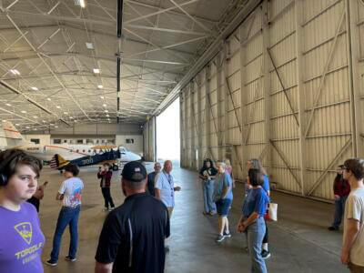 Un grupo de personas en el interior de un amplio hangar con un avión de fondo.