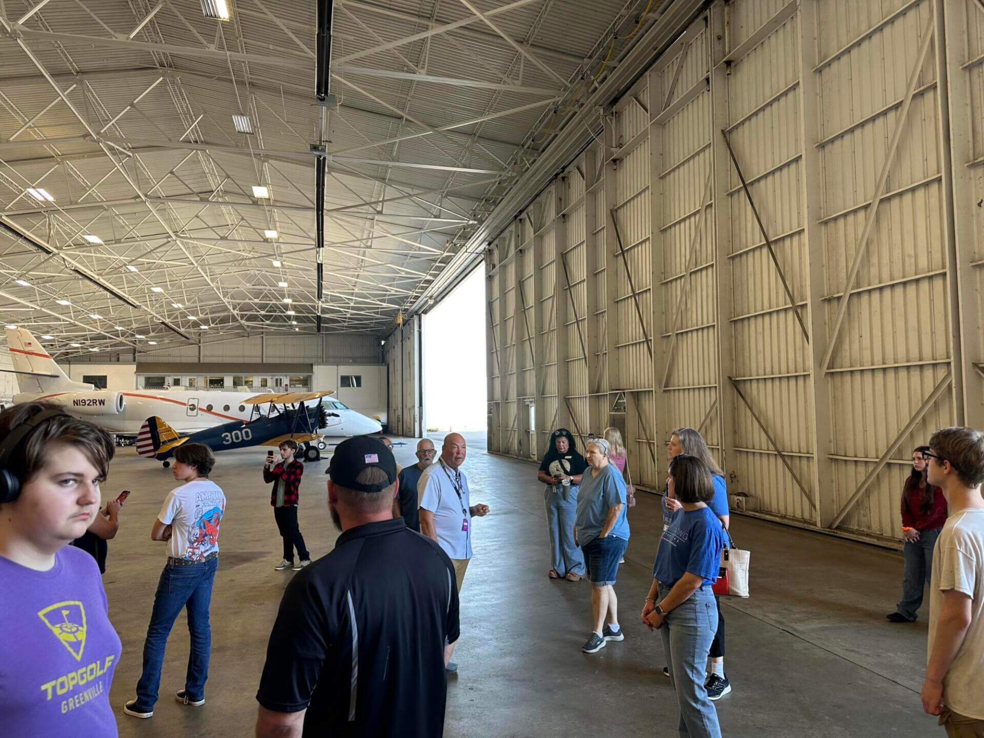 Un grupo de personas en el interior de un amplio hangar con un avión de fondo.