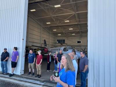 Un grupo de personas se encuentra ante un hangar abierto con una avioneta en su interior.