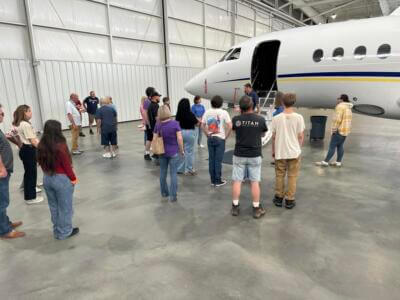 Un grupo de personas permanece atento cerca de un pequeño avión en un amplio hangar.