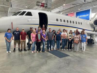 Un grupo de personas sonríe delante de un elegante jet privado en el interior de un hangar.