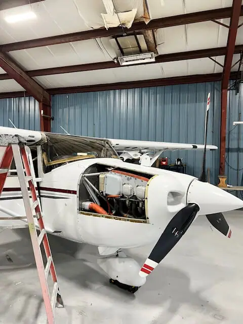 Un pequeño avión blanco dentro de un hangar, con un motor y una hélice a la vista.