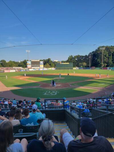 Partido de béisbol en un día soleado. Los aficionados sentados en un estadio observan a los jugadores en el campo.