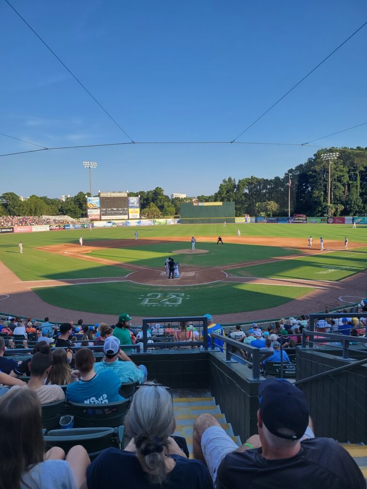 Partido de béisbol en un día soleado. Los aficionados sentados en un estadio observan a los jugadores en el campo.