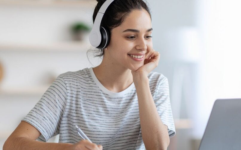 Estudiante con unos auriculares blancos mientras trabaja con su ordenador portátil.