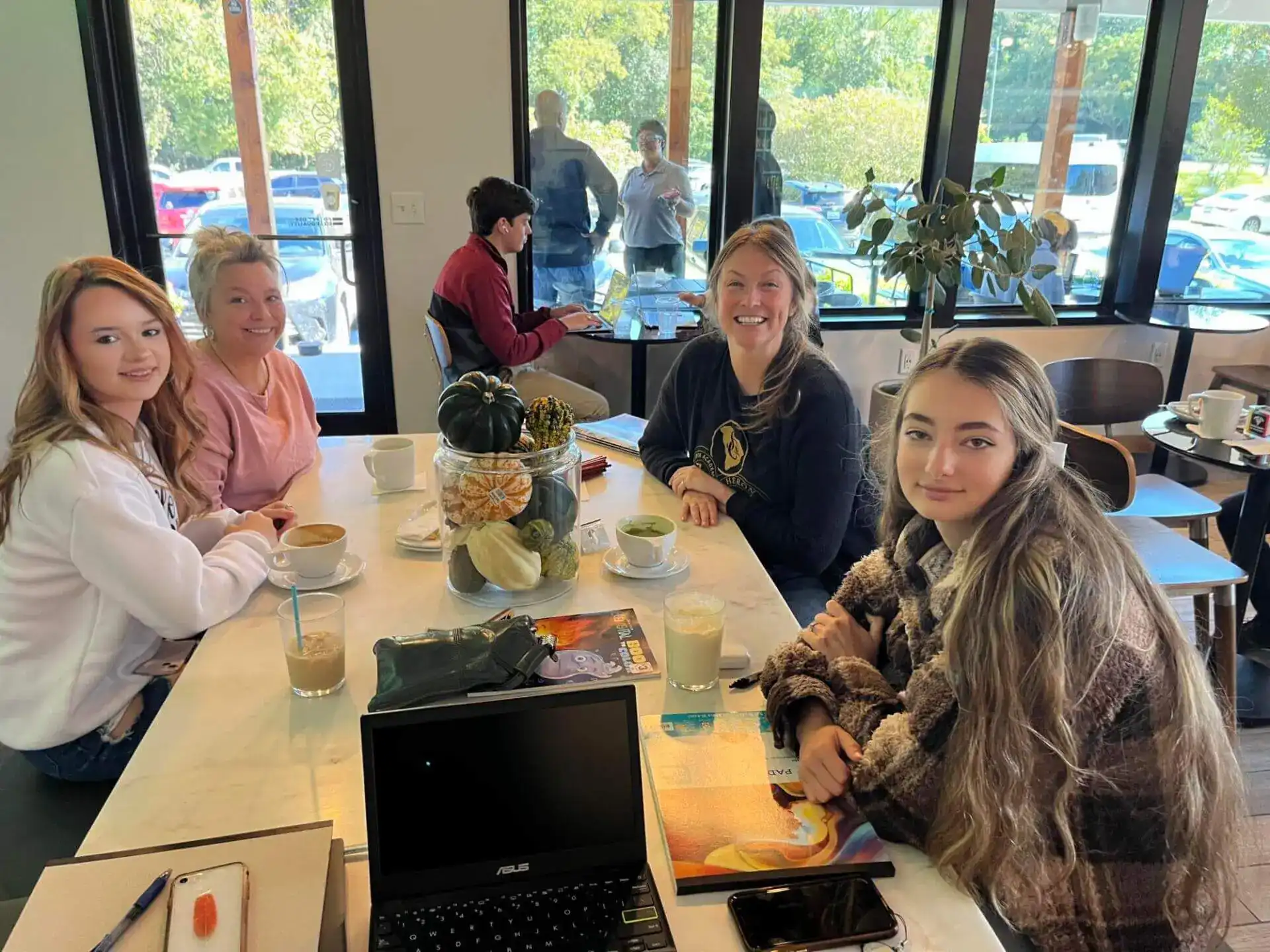 Cuatro personas sonríen alrededor de una mesa de cafetería con café y un portátil abierto