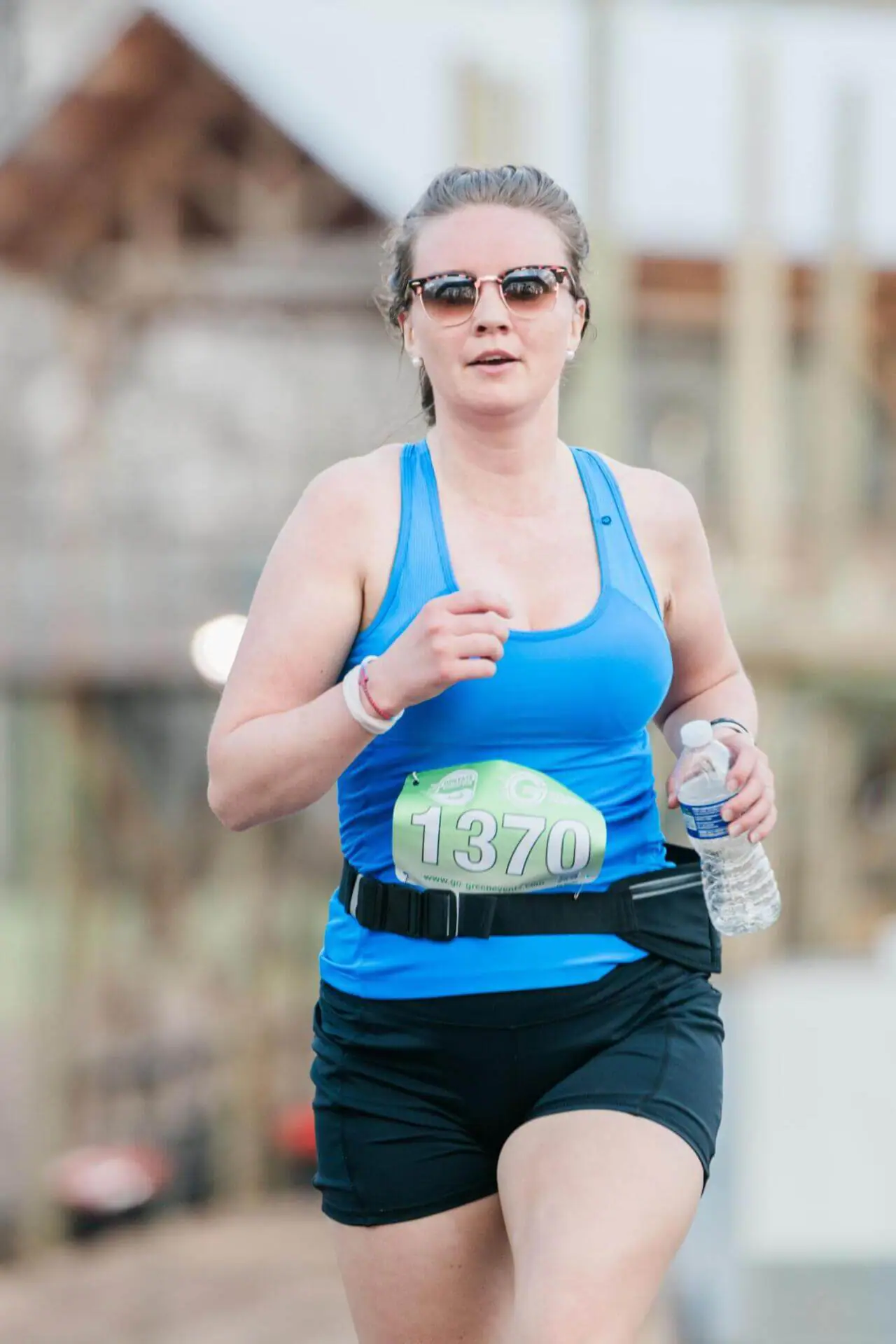 Mujer con gafas corriendo con una botella de agua en la mano