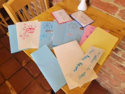 Sobre una mesa de madera se extienden diversas tarjetas hechas a mano con coloridos dibujos y mensajes.