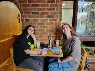 Dos personas se sientan a una mesa de madera en un acogedor café con paredes de ladrillo visto.
