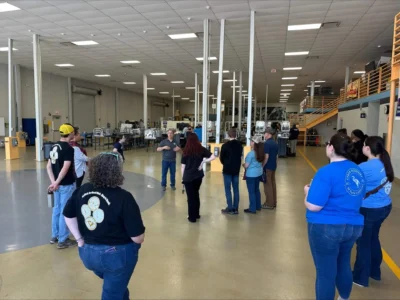 Un grupo de personas se encuentra en unas amplias instalaciones industriales, escuchando a un guía.
