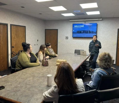 Un hombre, de pie al final de una mesa de conferencias, habla a cinco personas sentadas.