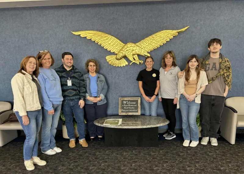 Un grupo de ocho personas sonríe ante una gran águila dorada en una pared azul.