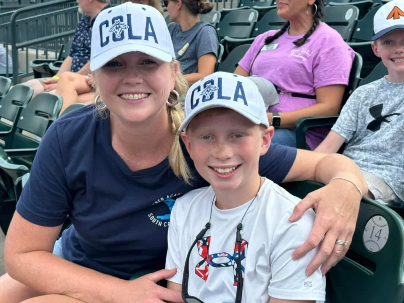 Una mujer y un niño sonrientes con gorras "COLA" a juego se sientan cómodamente en los asientos del estadio.